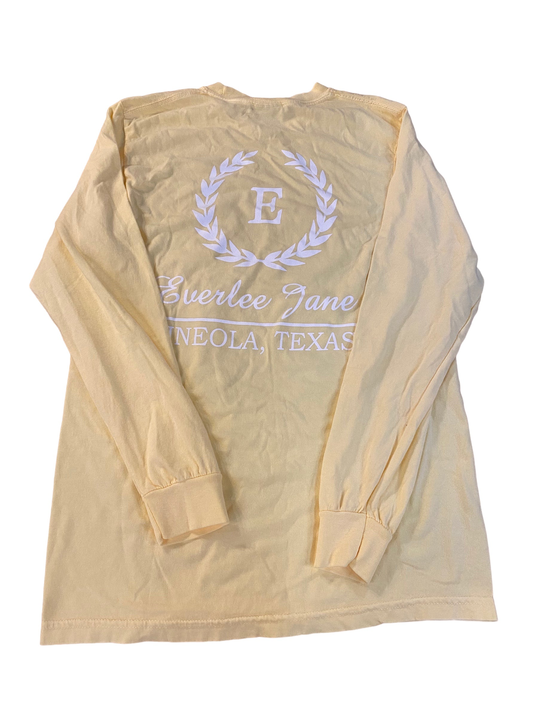 A beige long sleeve Everlee Jane T-Shirt LS with a printed emblem featuring the letter "e" encircled by a laurel wreath and the text "everlee jane, enola, texas" below it