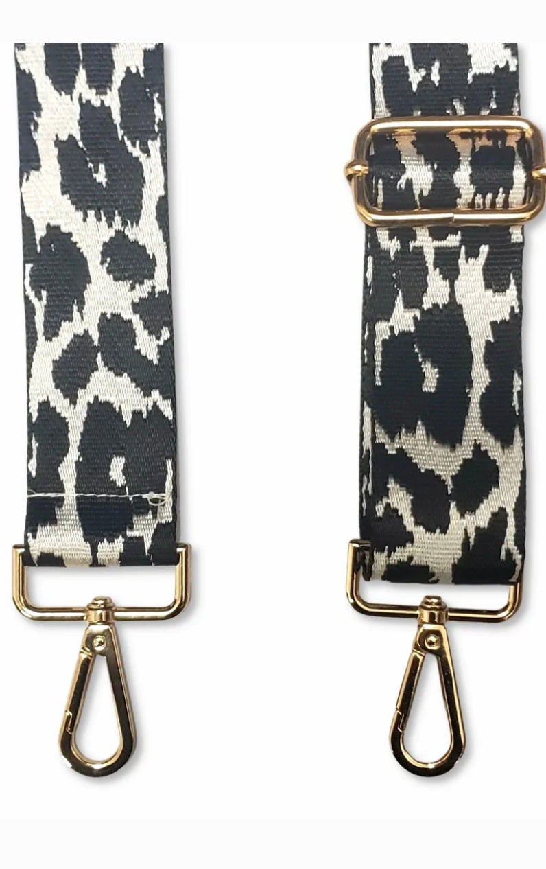 This product is a pair of Adjustable Crossbody Phone Straps in a black and white cow print design. Each strap features a gold buckle and gold clip at the ends. The straps allow for hands-free carrying of your phone. Fits all sizes.