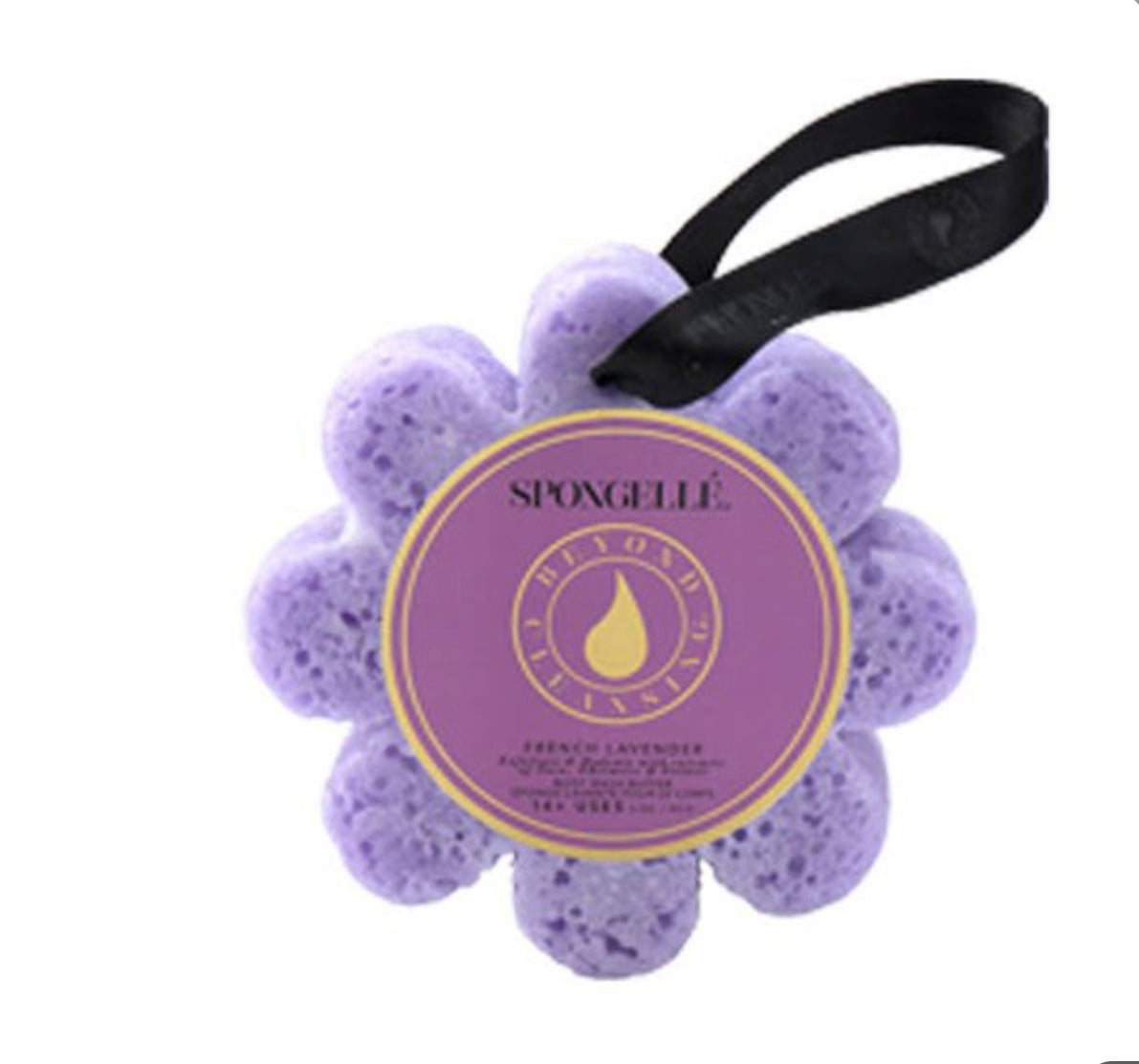 This is a Spongelle Flowers body wash buffer in vibrant purple. It's flower-shaped with a black ribbon for convenient use. The attached label indicates the soothing "French Lavender" scent. Enhanced with skin-moisturizing elements, it ensures gentle cleansing and hydration. Product size not specified.