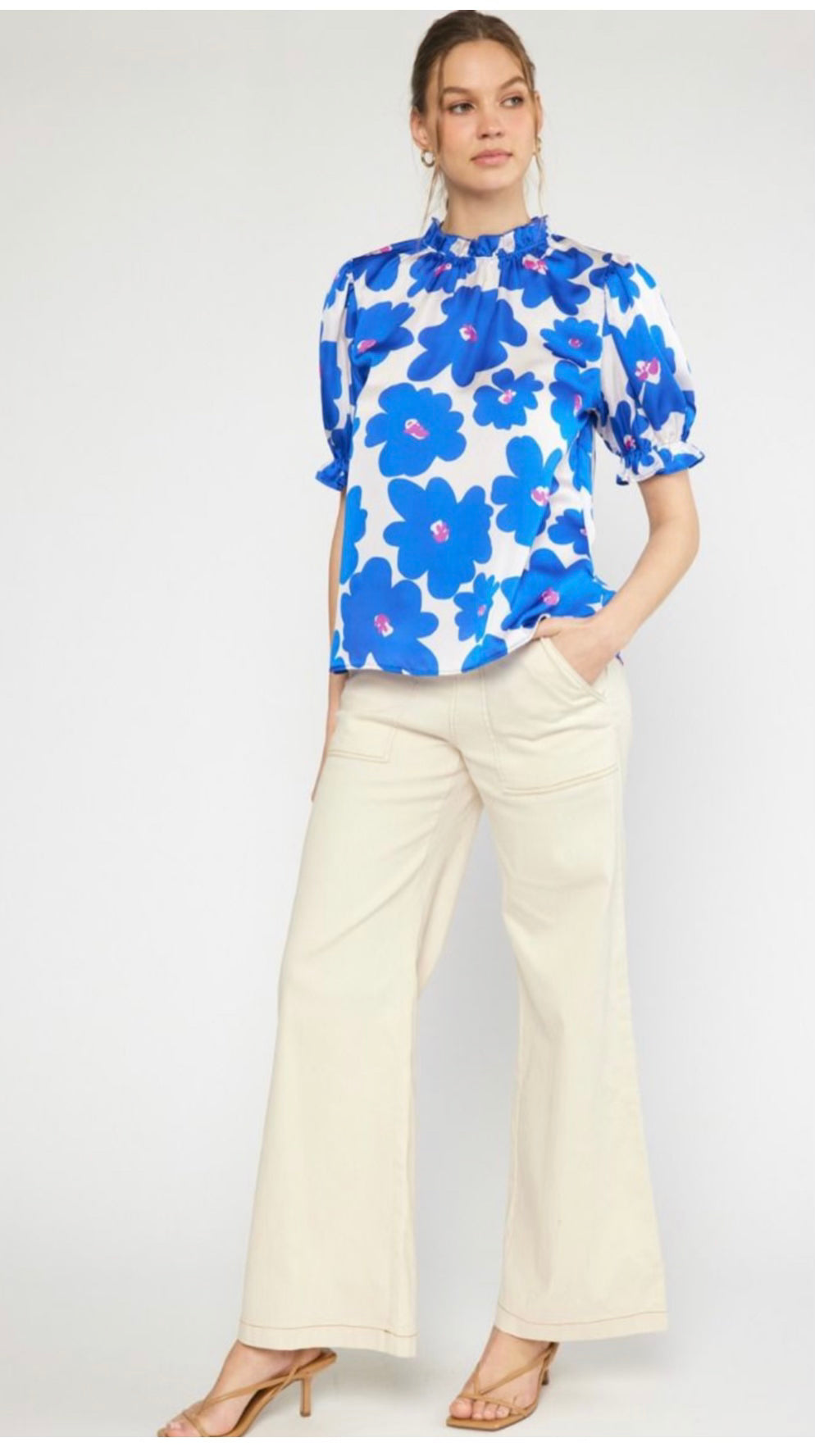 A woman poses with one hand on her hip, wearing a Cobalt Blue Ruffle Blouse and cream wide-leg trousers, paired with heeled sandals.