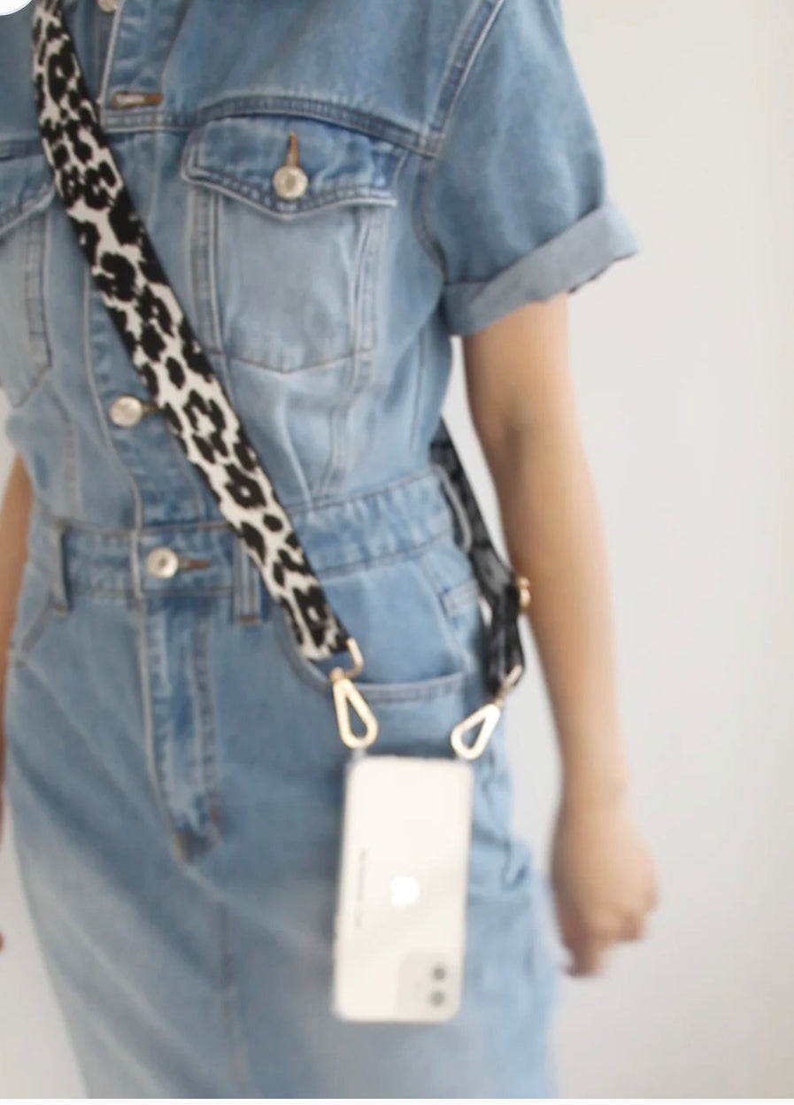 The product is a leopard print adjustable crossbody phone strap. It is designed to securely hold smartphones, shown here with a white smartphone. The strap length can be altered for comfort and style. Available in one universal size.