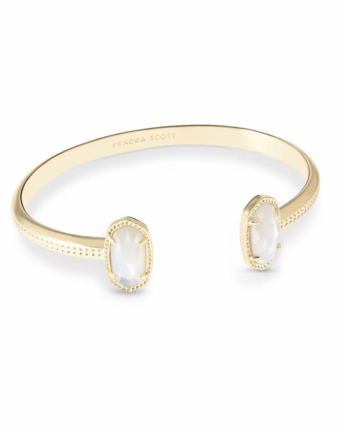Gold open cuff bracelet featuring two oval Ivory Mother-of-Pearl gemstones at each end, textured edge, and “KENDRA SCOTT” engraved on the adjustable inner band. Available in one adjustable size.