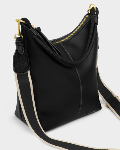 The Hallie Satchel Bag | Black is a vegan leather shoulder bag with gold zipper and hardware, and a wide black-and-beige striped fabric strap. Available in sizes small, medium, and large.