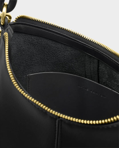 Close-up of the inside of the Hallie Satchel Bag in black with a gold zipper, interior pocket, suede lining, and “MADE IN ITALY” on the pocket. Available in small, medium, and large sizes.