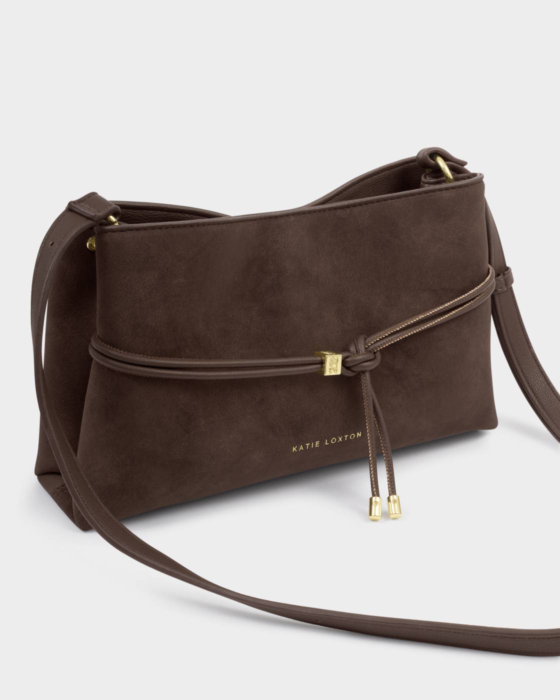 Brown faux suede crossbody bag with knotted front strap, gold-tone hardware, adjustable strap, and “Katie Loxton” engraving near the base. Available in one size.