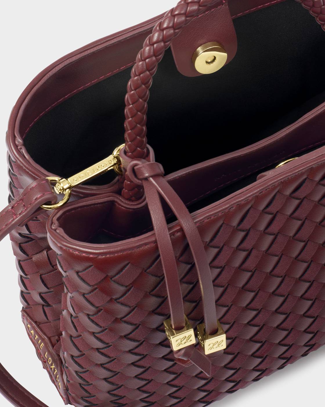 Nova Hand Woven Top Handle Bag in Cherry, burgundy vegan leather, gold hardware, braided handle, drawstring with gold accents, snap closure, black interior with brand label. Available in one size.