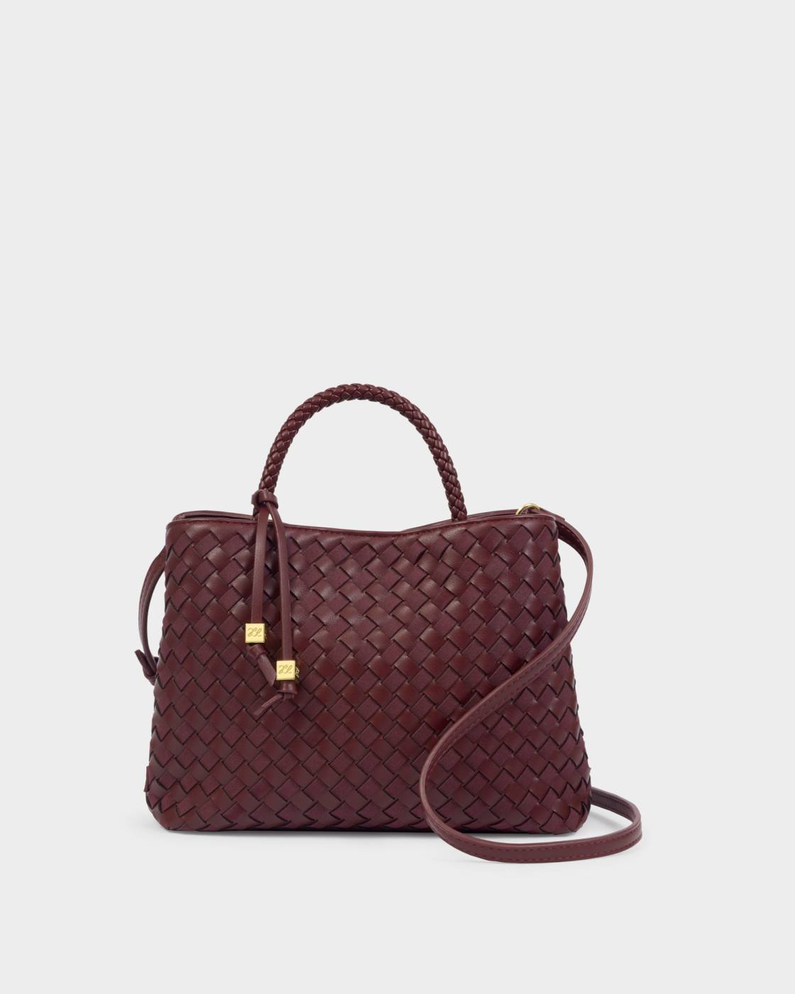 The Nova Hand Woven Top Handle Bag in Cherry features compact vegan leather with a woven texture, braided handle, crossbody strap, and gold-accented zipper pulls. Available sizes: small, medium.