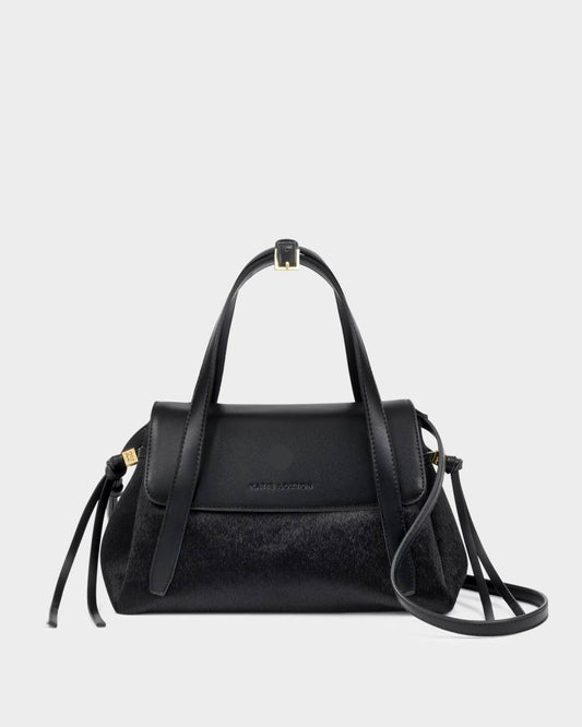 Alyssa Faux Pony Top Handle Bag in black faux pony hair and leather with gold hardware, top handle, detachable crossbody strap, flap closure, and side tassel details. Sizes available: [insert sizes].