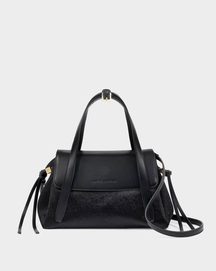 Alyssa Faux Pony Top Handle Bag in black faux pony hair and leather with gold hardware, top handle, detachable crossbody strap, flap closure, and side tassel details. Sizes available: [insert sizes].