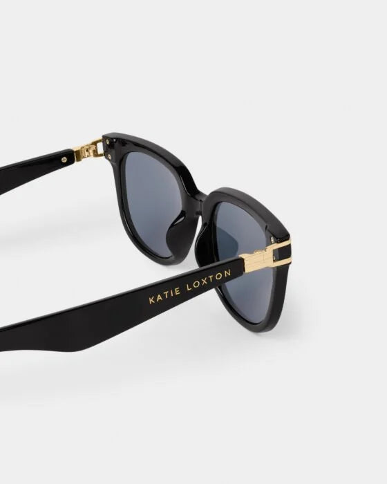 Manhattan Sunglasses: dark UV400 lenses, gold hinges, "KATIE LOXTON" on glossy black recycled frame. Sizes: S, M, L.