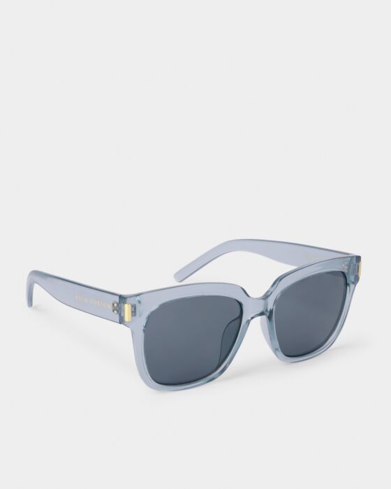 Roma Sunglasses: translucent light blue frames, dark UV400 lenses, wide arms, gold branding. Made from recycled materials. Sizes: S/M/L.