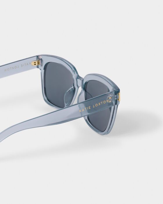 Roma Sunglasses: translucent blue, dark lenses, gold hinge accents, UV400. "KATIE LOXTON" in gold. Sizes: S, M, L.