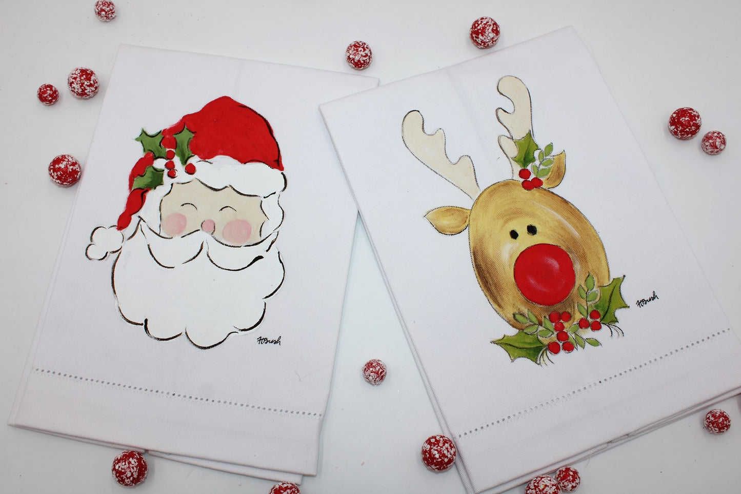 The 13"x20" Santa/Reindeer Handpainted Tea Towel set features two festive designs: a jolly Santa face and a cheerful red-nosed reindeer, embellished with holly leaves and decorative red and white balls. Perfect for holiday decor. Sizes available: 13"x20".