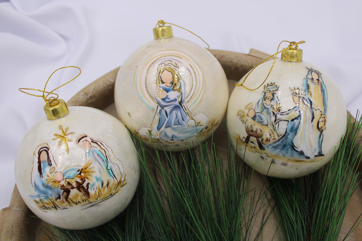 Three 4" handpainted Capiz ball ornaments featuring Nativity scenes, including Mary, Joseph, baby Jesus, and the Three Wise Men. Adorned with gold hanging loops.