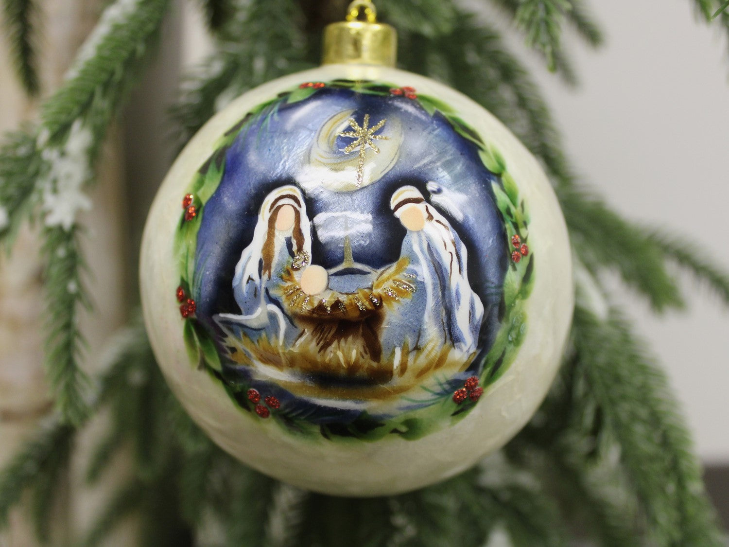 4" handpainted Capiz ball ornament illustrating the Nativity scene with Mary, Joseph, and baby Jesus, encircled by a wreath design with a star above.