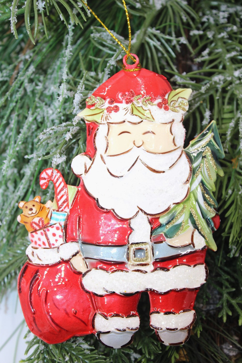 Handpainted Molded Metal Santa Ornament (3.75x5.25") features Santa with a green tree, teddy bear, and candy cane in a red sack; snow-dusted branches shimmer beautifully.