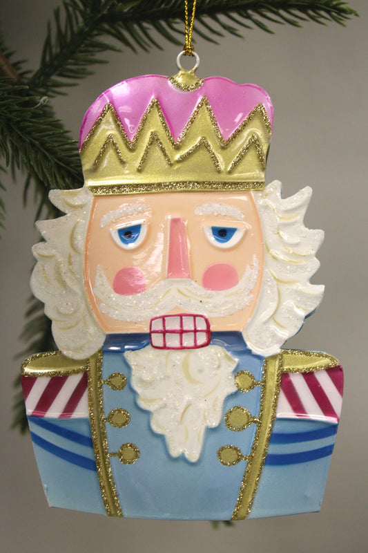 Handpainted molded metal nutcracker ornament, 3.75"x0.75"x5.25", with white beard, pink crown, and blue-gold uniform.