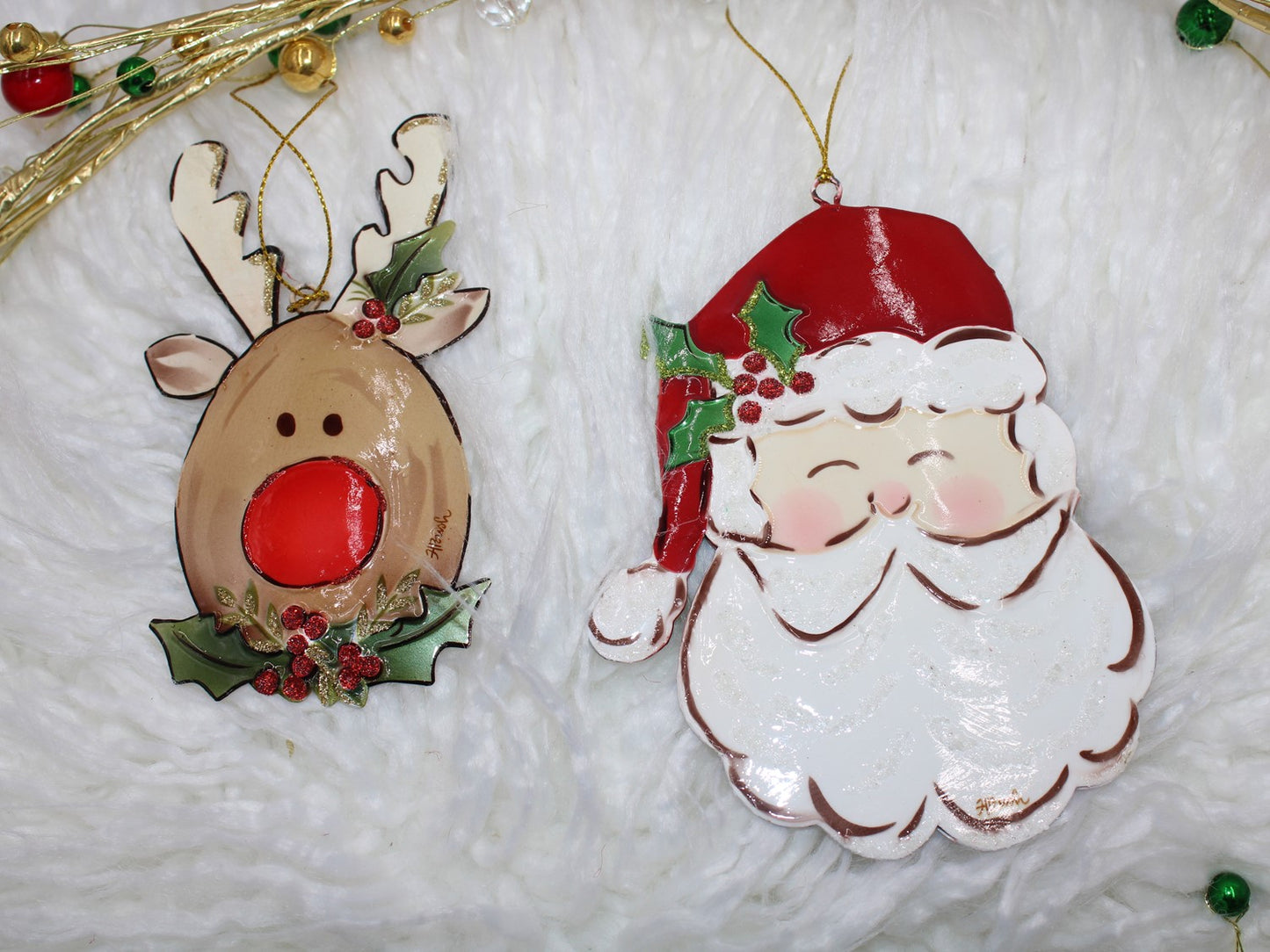 The Handpainted Molded Metal Ornaments feature a cartoon reindeer with a red nose and holly, and a jolly Santa Claus face with a red hat and white beard. Perfect for holiday decor. Available in one size.