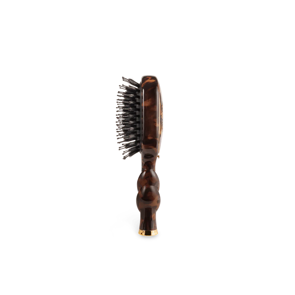The Mini Boar Brush | Tortoise features black boar bristles with a patterned handle; available in compact travel size.