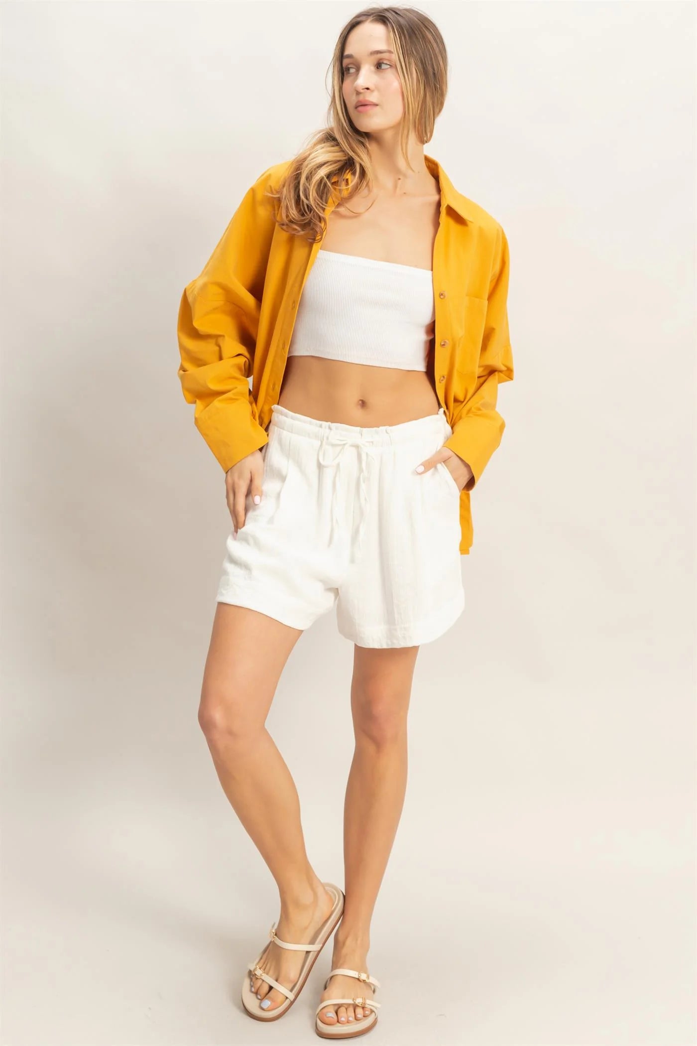 Beige drawstring pleated shorts, available in sizes XS–XL. Features adjustable waist and side pockets.