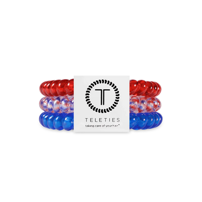 Three TELETIES Hair Ties—red, clear with blue, and blue—in branded white packaging. Available in small and large sizes.