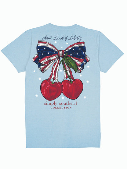 Light blue tee with American flag bow, two cherries, text above and below. Available in sizes S-XXL.