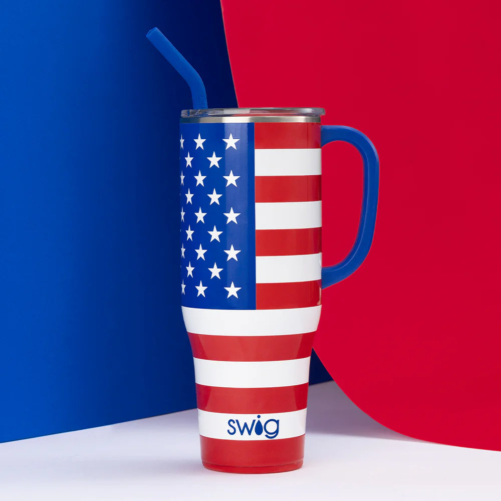 Tall tumbler with comfort-grip handle and reusable straw, decorated with patriotic stars and stripes American flag design. Brand name "Swig" printed on the bottom. Available in sizes: 22 oz, 32 oz.