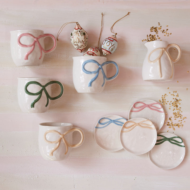 Handcrafted pastel ceramic mugs and plates with raised ribbon and bow accents. Available in multiple sizes.