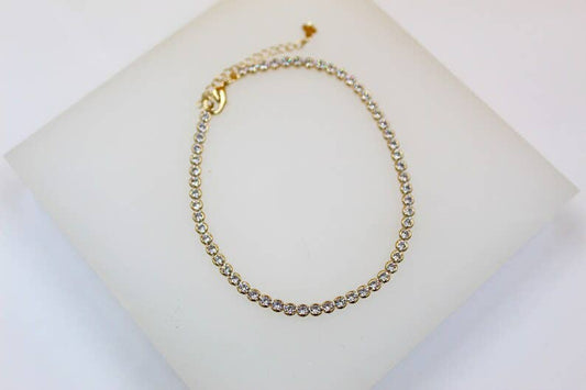 The product is an 18K gold-filled Tennis bracelet. It features a 3mm diameter and is adorned with numerous CZ stones throughout its length. Its design includes a functional clasp on one end. The bracelet is displayed on a pure white surface for viewing clarity.