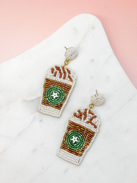 Nickel-free beaded earrings shaped like iced coffee cups with green logos and whipped cream. Available in one size.