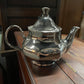 Silver teapot with a curved handle and spout; reflective surface. Available sizes: small, medium, large.