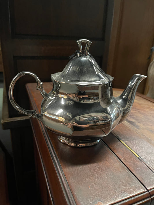Silver teapot with a curved handle and spout; reflective surface. Available sizes: small, medium, large.