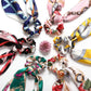 Seven vintage floral scarf scrunchies with vibrant patterns and scarf-like tails. Available in one-size fits all.