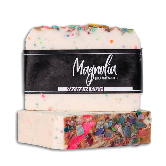 Birthday Party Soap from Magnolia Soap and Bath Co. Appears as a stack of two bars with colorful, sprinkle-like embeds. Infused with a unique birthday fragrance. Labeled "birthday cake". Comes exclusively in standard soap bar size.