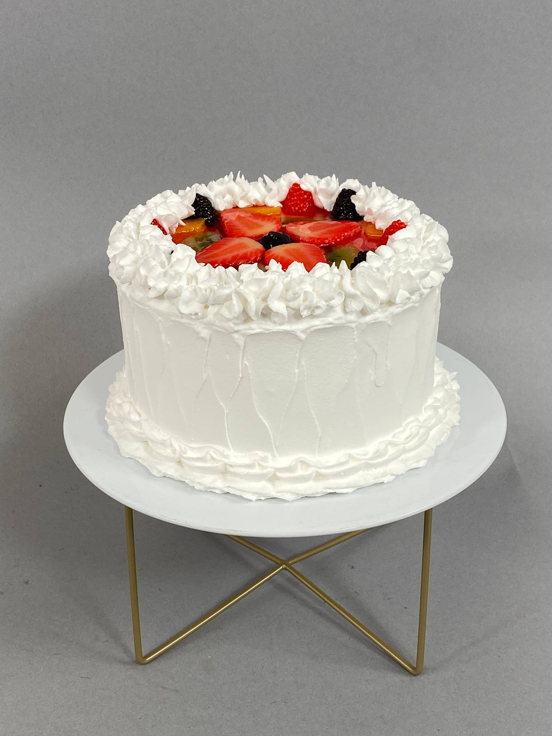 Small fake vanilla cake with white frosting and faux fruit topping. Available in small size only.