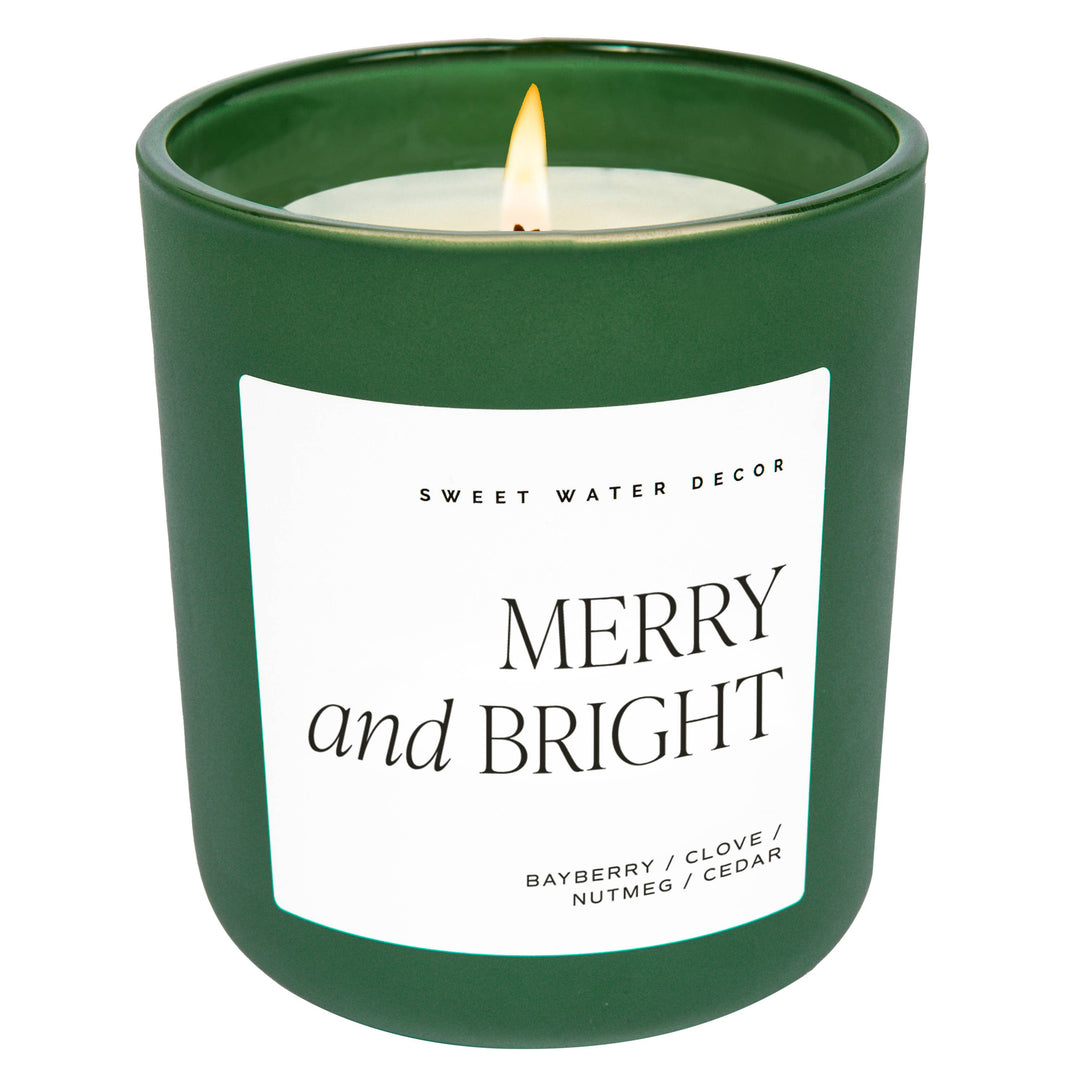 Lit Merry and Bright 15 oz soy candle in a matte green glass jar with bayberry, clove, nutmeg, and cedar scents.