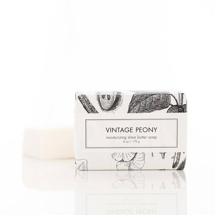 The Vintage Peony Shea Butter Soap from Formulary 55 is a luxurious bath bar wrapped in intricately designed white packaging featuring delicate botanical illustrations. The soap itself offers an elegant vintage peony scent, enhanced by the moisturizing properties of shea butter. Ensures a soothing and nourishing bathing experience. Available in one standard bar size.
