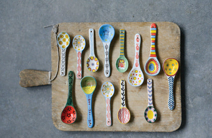 Fourteen hand-painted stoneware spoons with unique patterns, available in various sizes.