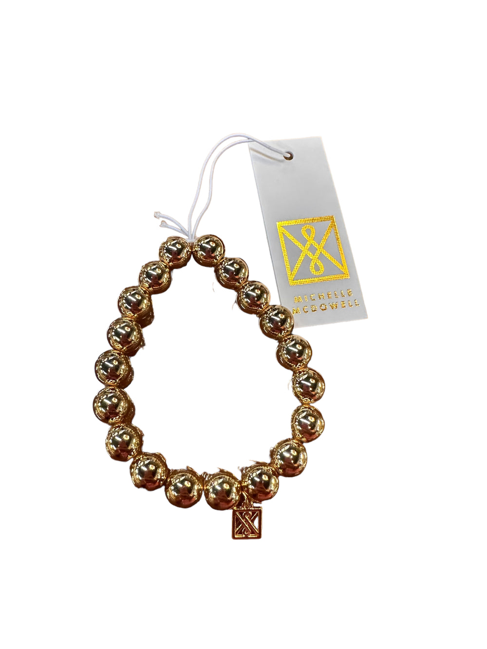 Shiny gold beaded bracelet with rectangular charm, white/gold tag "Mcenlis Rogovskis". Available sizes: S, M, L.