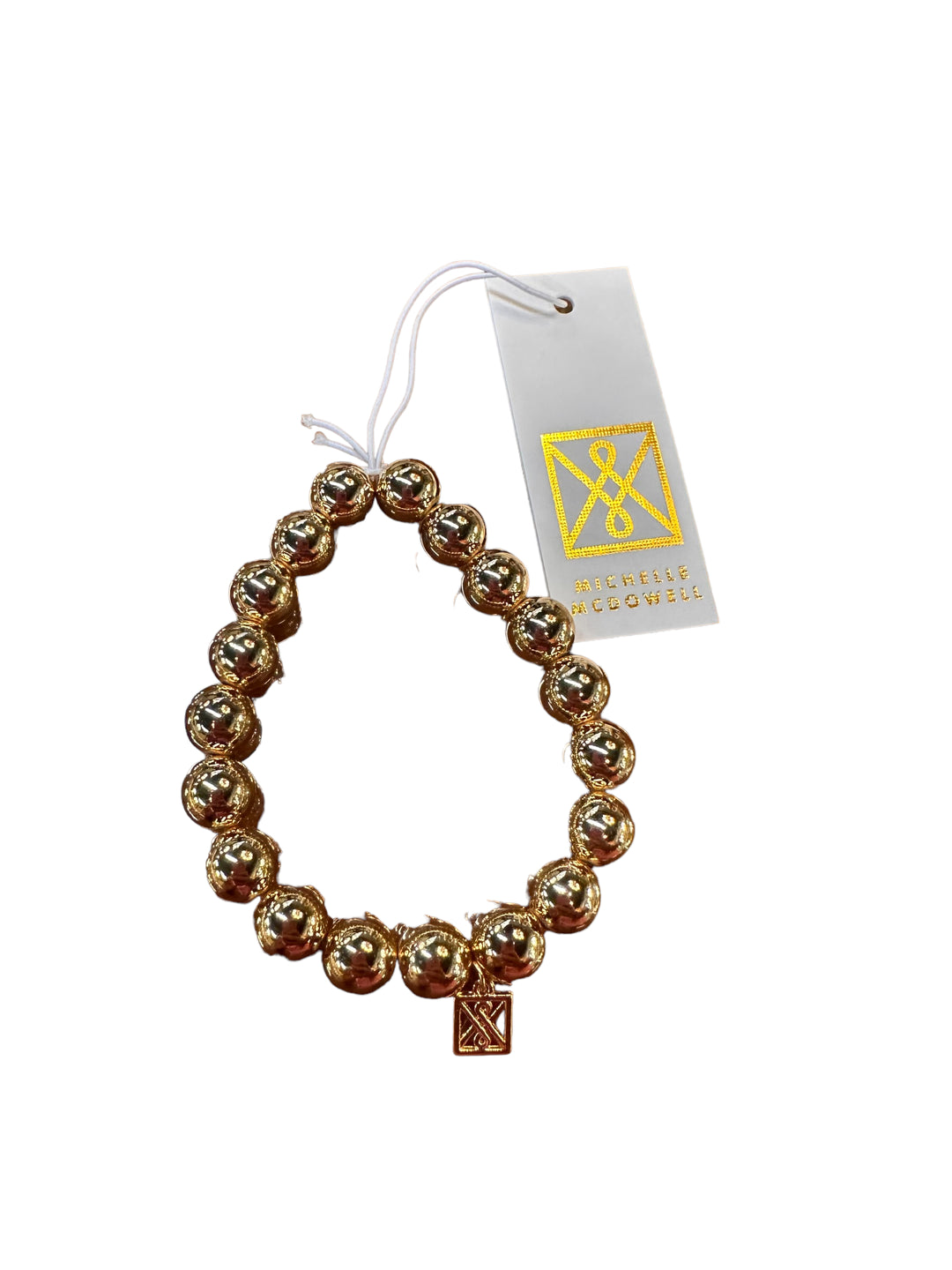 Shiny gold beaded bracelet with rectangular charm, white/gold tag "Mcenlis Rogovskis". Available sizes: S, M, L.