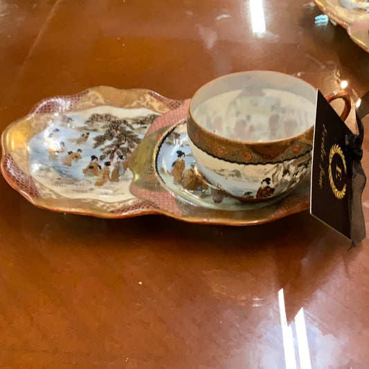 Decorative porcelain teacup and saucer with painted scenes; black tag with gold detail. Sizes available: not specified.