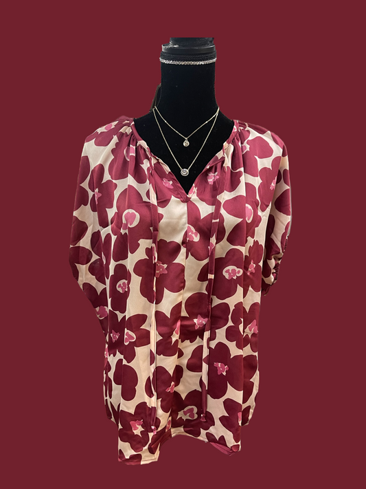 The Wine Floral Blouse comes in small, medium, and large sizes. It features a pink and burgundy floral pattern on silk-like fabric. The blouse is also styled with a delicate necklace.