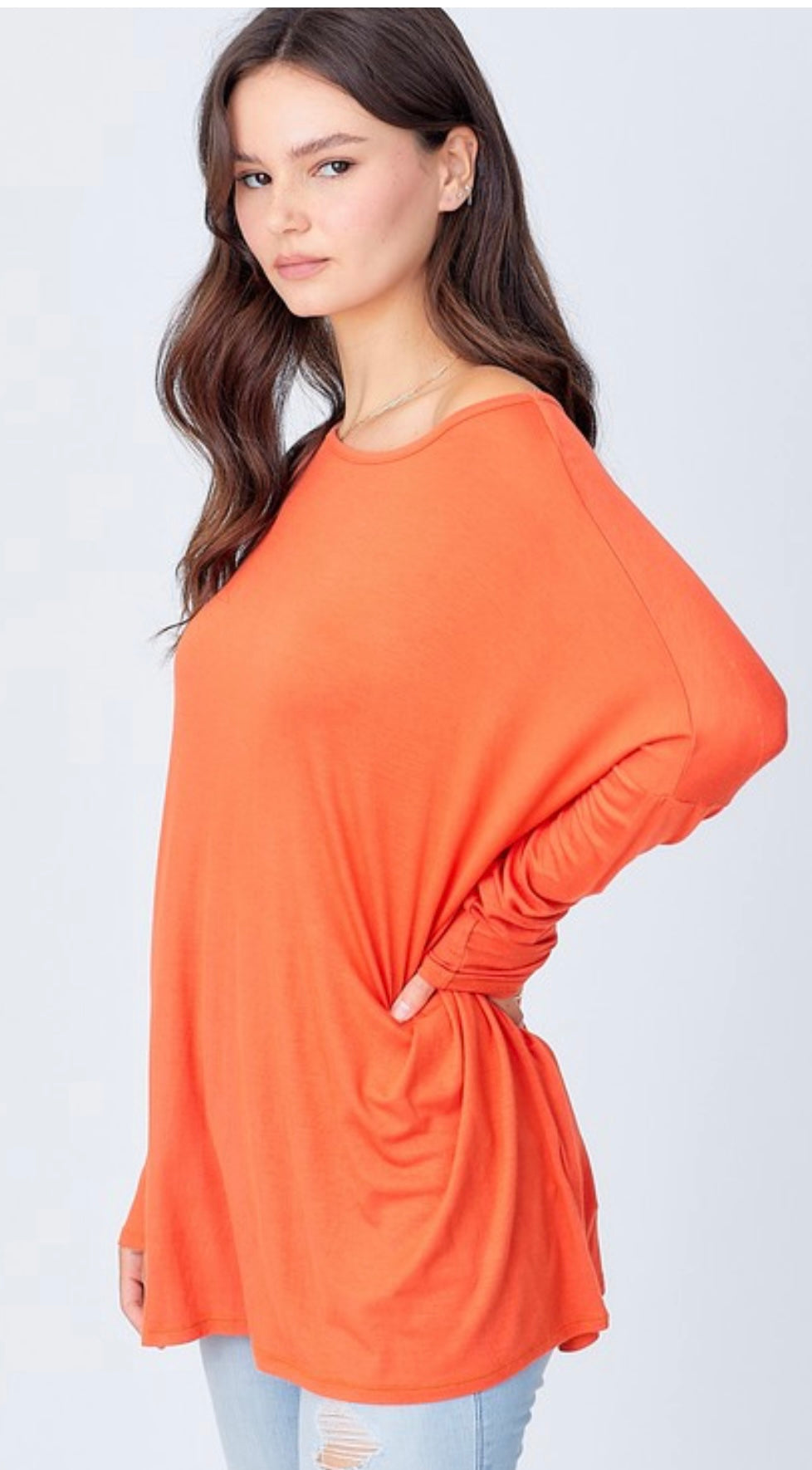 A young woman wearing an A.gain “The Perfect Shirt” Long Sleeve Regular in bright orange and jeans, standing sideways with her hand on her hip and looking at the camera.