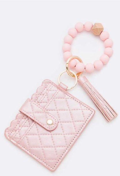 Light pink quilted wristlet wallet with snap, keyring, beaded bracelet, and tassel. Available in one size. Nickel compliant.
