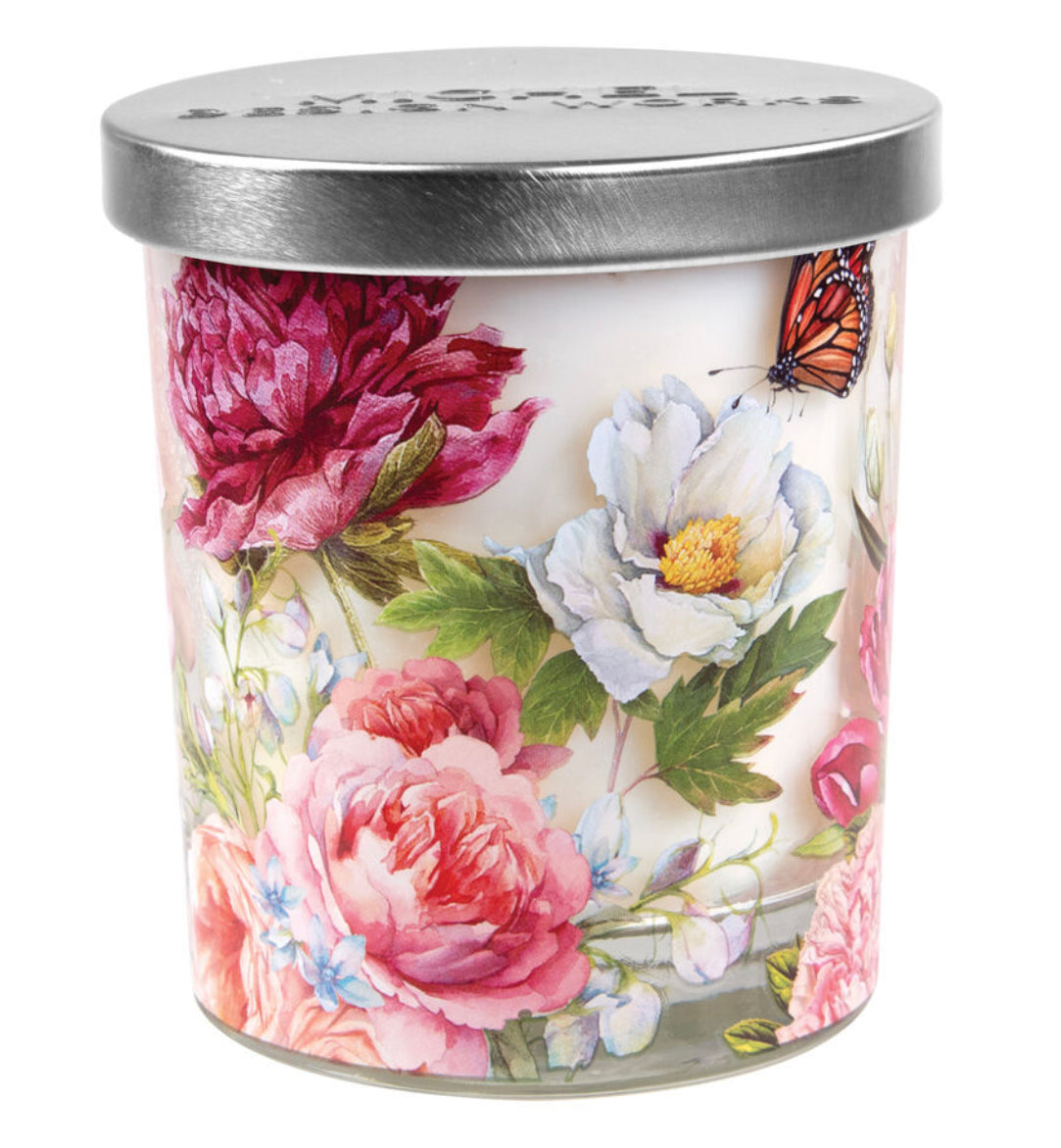 The Blush Peony Candle Jar is a decorative candle in a glass container with a silver lid, featuring a vibrant floral design of roses, gardenias, and peonies, plus a butterfly. Available sizes: Small (6 oz), Medium (12 oz), Large (18 oz).