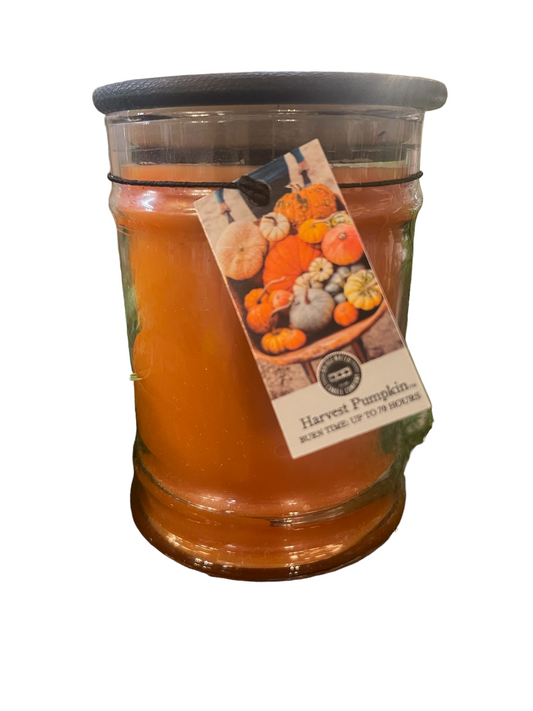A glass jar candle labeled "Harvest Pumpkin" with a clear orange wax. There's a label featuring pumpkins and gourds attached to the jar with a small black clip.
