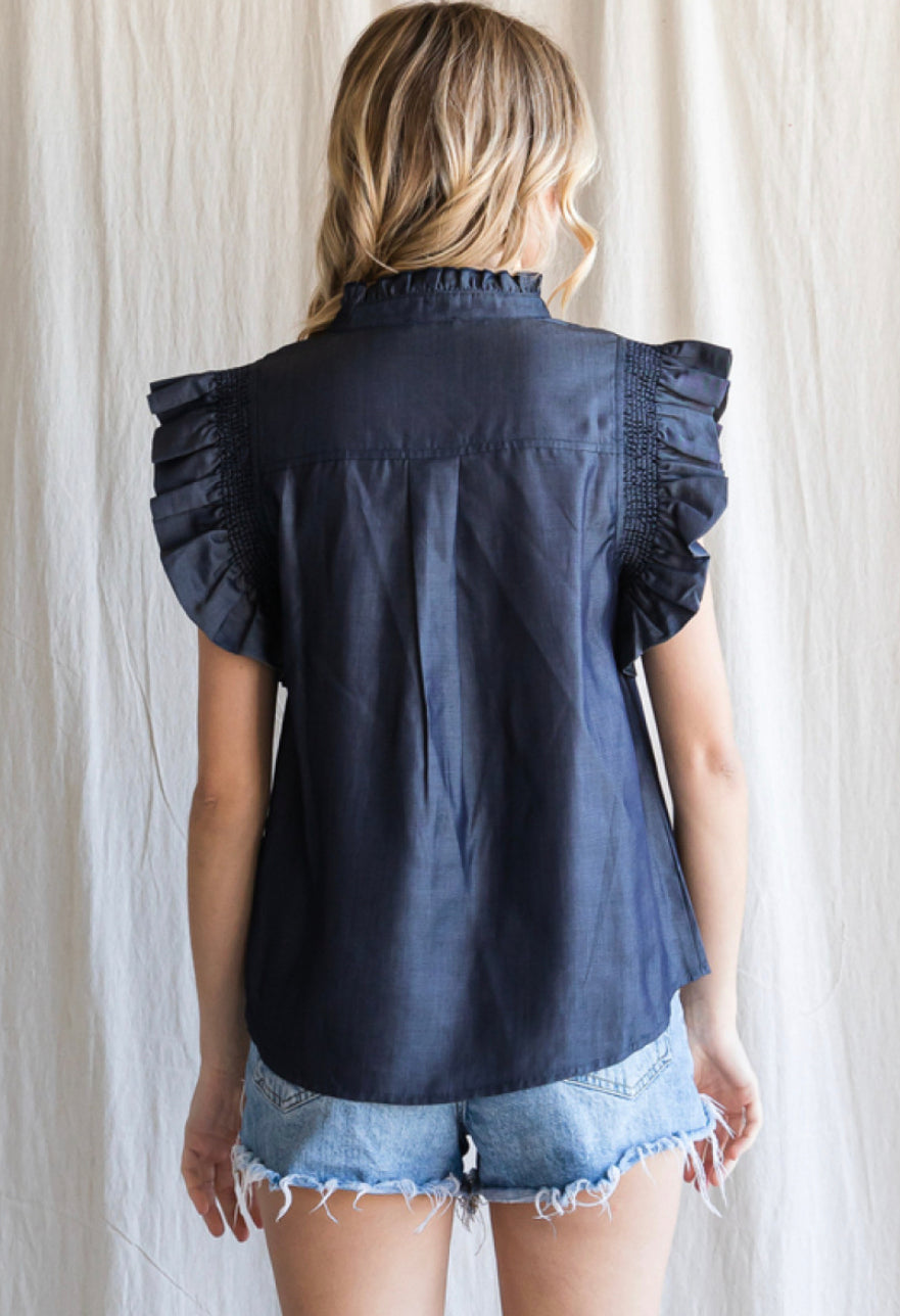 A woman seen from behind wearing a Denim Frilled Top with smocked frilled shoulders and distressed denim shorts, standing in front of a neutral backdrop.