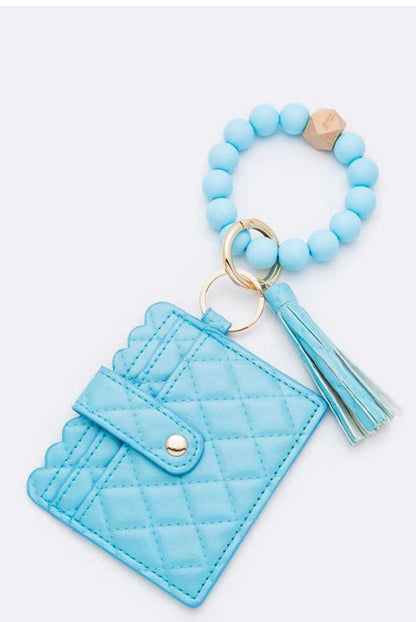 Light blue quilted card case with button clasp, keyring with blue beads, gold ring, wooden bead, and tassel. Sizes: S/M/L.