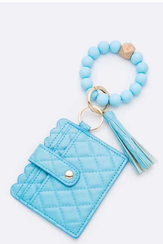 Light blue quilted card case with button clasp, keyring with blue beads, gold ring, wooden bead, and tassel. Sizes: S/M/L.