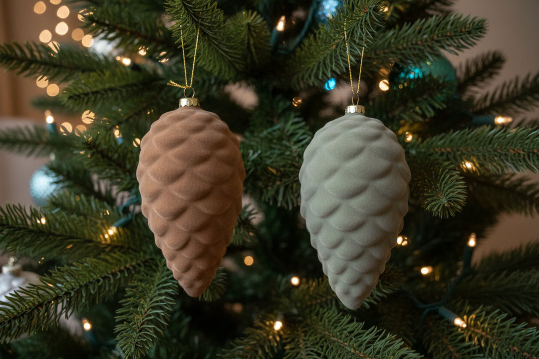 This product includes two Flocked Glass Pinecone ornaments, measuring at 6 1/2" H each. The set provides one in a beautiful taupe color and the other in a sleek gray hue.